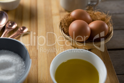 Eggs in wicker basket with oil, and sugar on wooden board