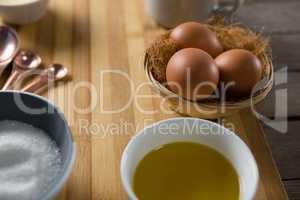 Eggs in wicker basket with oil, and sugar on wooden board