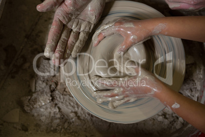 Male potter assisting his daughter in making a pot