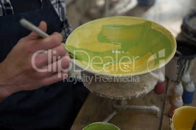 Male potters hand painting a bowl in pottery workshop