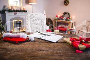 Wrapped gift, santa hat, diary and quill pen on wooden table in living room