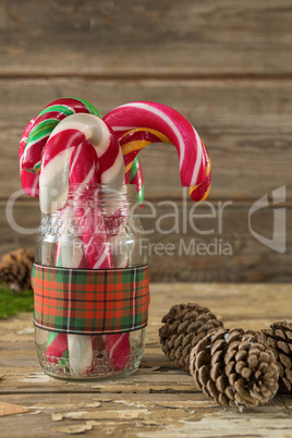 Pine cones and candy cane in jar against wooden plank