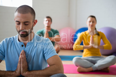 Yoga instructor with students meditating in prayer position at club