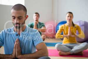 Yoga instructor with students meditating in prayer position at club
