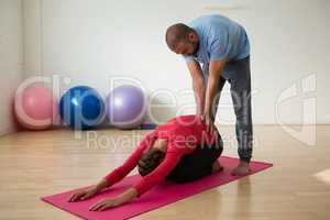 Instructor assisting student in doing child pose at studio