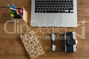 Laptop, camera, spectacles, notepad and pencil holder on wooden plank