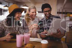 Man showing laptop to cheerful female friends at coffee shop