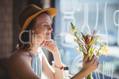 Smiling young woman looking at flower against window