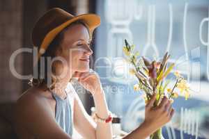 Smiling young woman looking at flower against window
