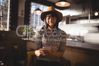 Smiling beautiful female customer using mobile phone at coffee shop