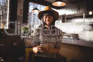 Smiling beautiful female customer using mobile phone at coffee shop