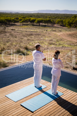 Couple practicing yoga on at poolside