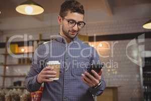 Businessman having coffee while using phone in cafe