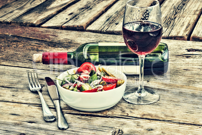 Ordinary French lunch. Red wine and a salad of fresh vegetables in a white bowl.
