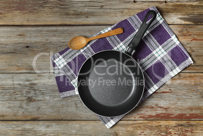 Empty frying pan on a wooden background with a kitchen napkin