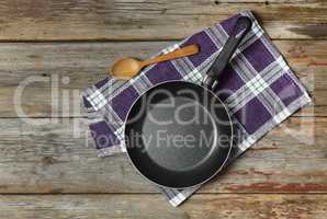 Empty frying pan on a wooden background with a kitchen napkin