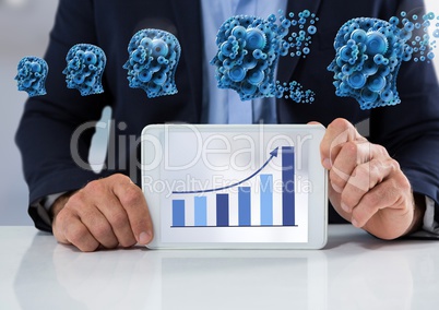Businessman with tablet at desk with diagram of bar chart and cogs heads