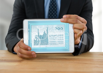 Businessman with tablet at desk with diagrams and charts