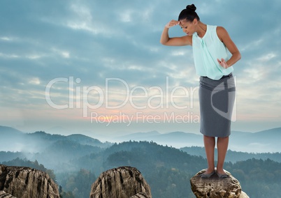 Businesswoman looking down from height on rock in mountains