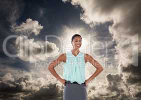 Businesswoman with hands on hips in front of clouds