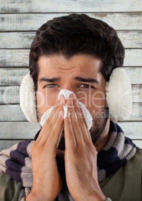 Man against wood with ear muffs and blowing nose in tissue