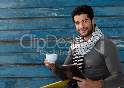 Man against wood with warm scarf and cup and tablet
