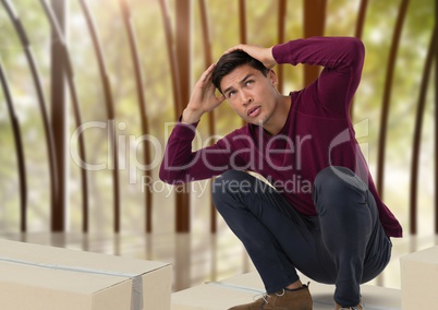Man holding head and crouched small on boxes by windows