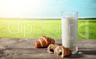 Glass of milk on rustic table with croissants