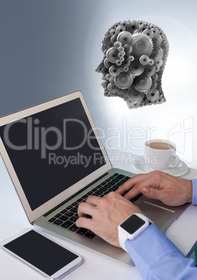 Businessman with laptop and phone at desk with cogs head