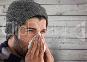 Man against wood with warm hat blowing nose in tissue