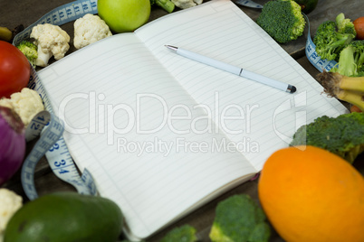 Open diary with vegetables on wooden background