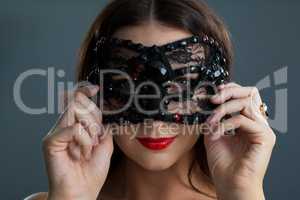 Woman wearing masquerade mask against black background