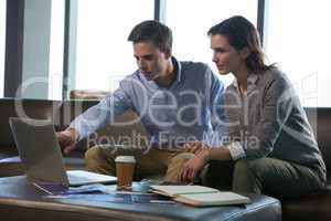 Male executive and female executive discussing over laptop