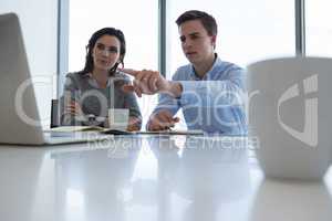 Male executive and female executive discussing over laptop