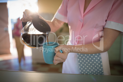 Waitress pouring black coffee in mug at restaurant