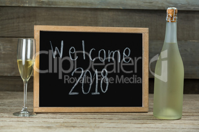 Champagne bottle and glass kept beside the slate with welcome 2018