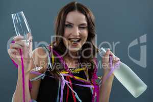 Smiling woman wrapped in multi color streamers holding champagne bottle and glass