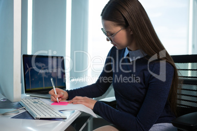 Female executive writing on sticky note at desk