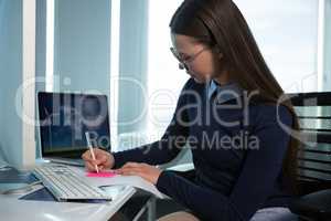 Female executive writing on sticky note at desk