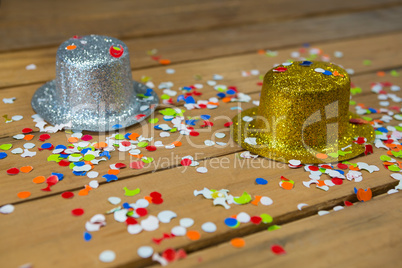 Golden and silver hat with confetti on wooden surface