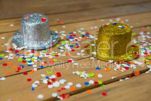 Golden and silver hat with confetti on wooden surface