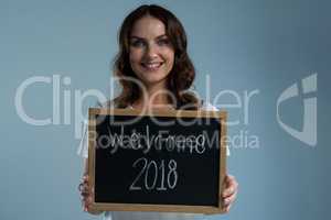 Smiling woman showing slate with text welcome 2018 against grey background