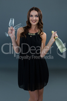 Smiling woman holding champagne bottle and two glass against grey background