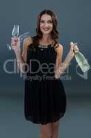 Smiling woman holding champagne bottle and two glass against grey background