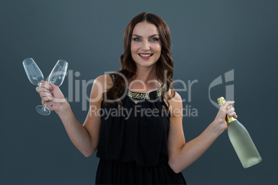 Smiling woman holding champagne bottle and two glass against grey background