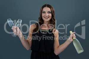 Smiling woman holding champagne bottle and two glass against grey background