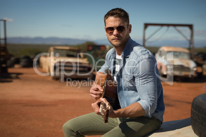 Man playing guitar while sitting on a car