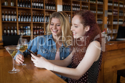 Female friends using mobile phone while having drinks in bar