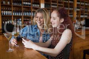 Female friends using mobile phone while having drinks in bar