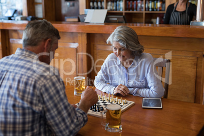 Friends playing chess while having glass of beer in bar